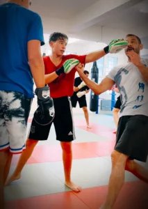 Boxtrainer im Combat Club zeigt einem jungen Schüler eine Boxübung an der Pratze